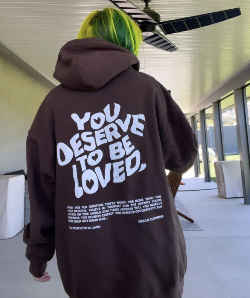 Back of a brown DREAM hoodie with ‘You Deserve To Be Loved’ printed in white.