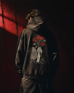 Person wearing a black Dreams Never Die rose hoodie in dramatic red light
