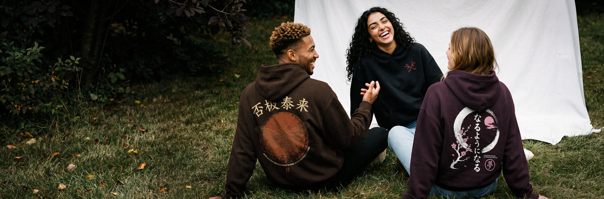 Three friends laughing on the grass wearing DREAM hoodies