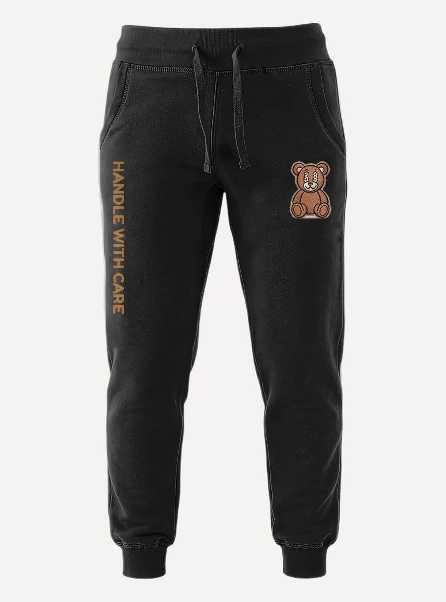 Handle With Care black joggers, front view — brown Handle With Care leg print and Somni bear patch