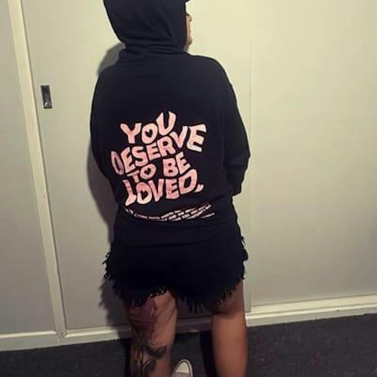 Customer wearing You Deserve To Be Loved black hoodie, back print visible, hood up