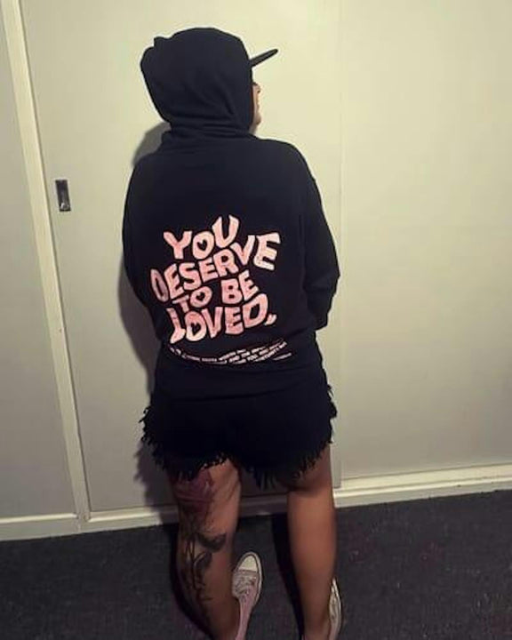 Customer wearing You Deserve To Be Loved black hoodie, back print visible, hood up